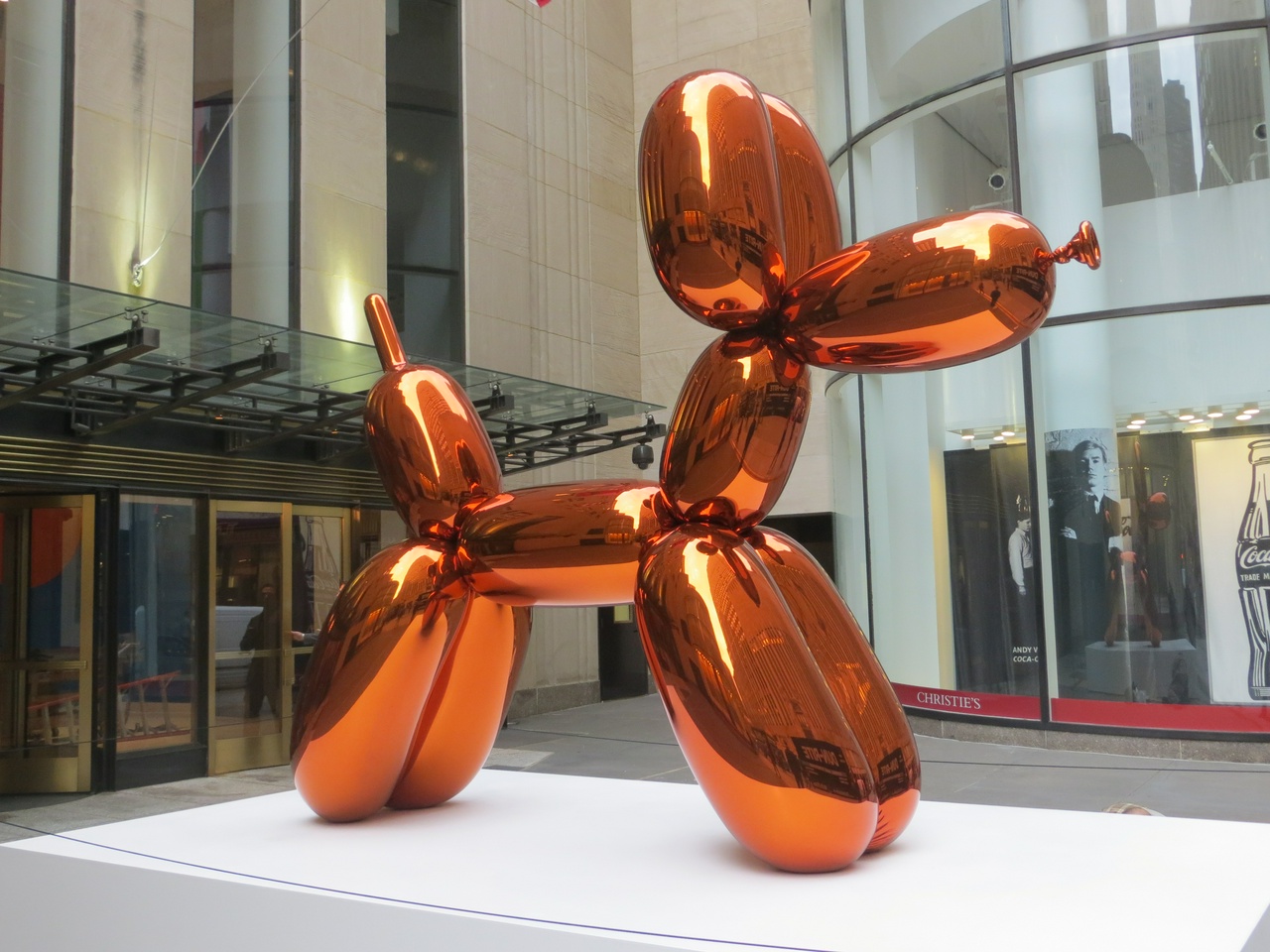 Escultura de Jeff Koons representando un perrito de globos, color naranja brillante, sobre un pedestal blanco, en un muso.
