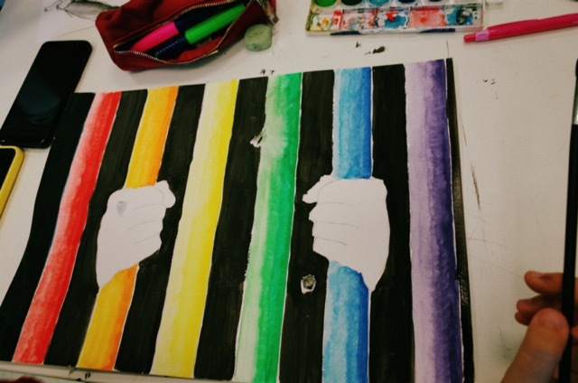 Una pintura de unos manos detras de unos barrotes de colores.